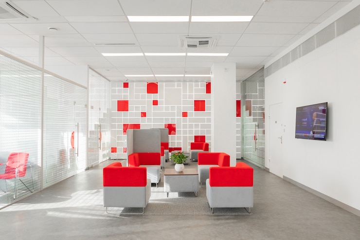 Foto angolo dell&#39;ufficio moderno con pareti bianche, pavimento grigio, area open space con poltrone rosse e bianche e stanze dietro la parete di vetro