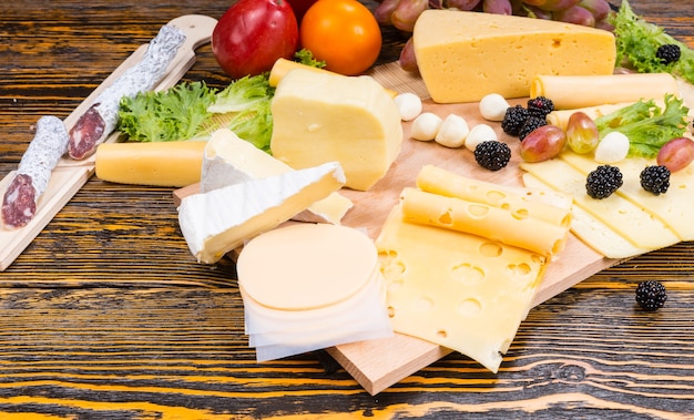 Angolo di Alta Vista di Gourmet Cheese Board con varietà di formaggi, salumi e frutta fresca servita su tavola in legno rustico con venature del legno e spazio di copia