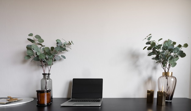 Angolo di lavoro della camera da letto con il computer portatile, le candele bianche e la pianta artificiale sulla tavola di lavoro di legno nera.