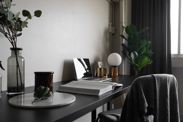 Angolo di lavoro della camera da letto decorato con le candele bianche del computer portatile e la pianta artificiale in vaso di vetro sulla tavola di lavoro di legno con la parete dipinta beige