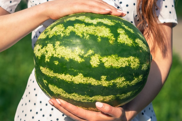 Anguria intera da vicino nelle mani della giovane donna su sfondo verde natura.