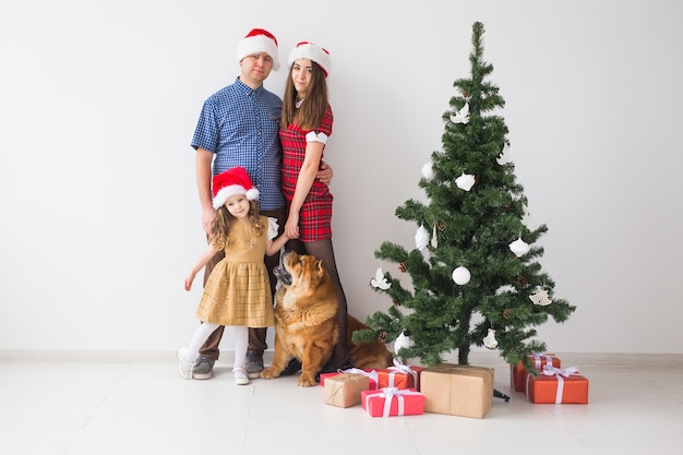 Animale domestico, vacanze e concetto festivo - La famiglia con il cane è in piedi vicino all'albero di Natale.