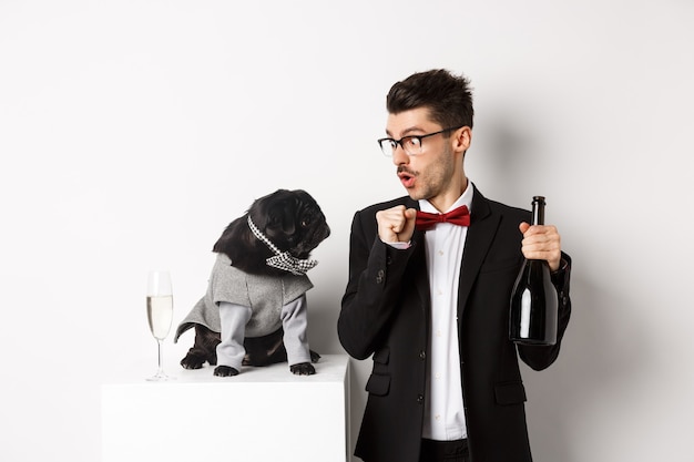 Animali domestici, vacanze invernali e concetto di Capodanno. Felice giovane uomo che celebra il Natale con il simpatico cane nero che indossa il costume da festa, cucciolo guardando il proprietario, bianco.