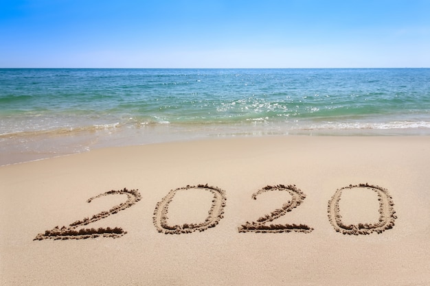Anno 2020 scritto sulla spiaggia di sabbia con acqua delle onde del mare