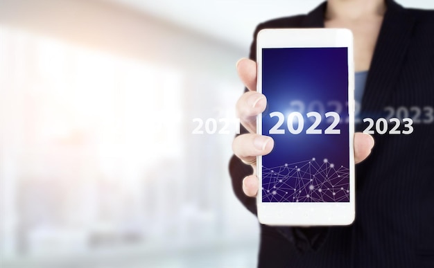 Anno nuovo concetto. Tenere in mano lo smartphone bianco con l'ologramma digitale 2022 segno su sfondo sfocato chiaro. 2022 anno nuovo. Anno duemilaventidue concetto.