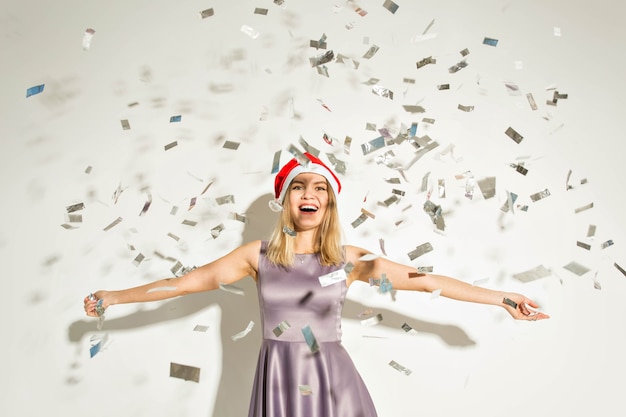 Anno nuovo e concetto di vacanze - Felice giovane donna eccitata con cappello di Babbo Natale che balla e ride su sfondo bianco.