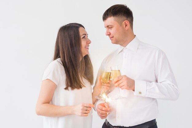 Anno nuovo, festività, data e concetto di San Valentino - Coppia di innamorati che tengono la luce delle stelle filanti e bicchieri di champagne su sfondo bianco