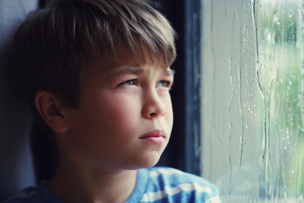 Annoiato di essere annoiato Inquadratura di un ragazzo triste che guarda la pioggia attraverso una finestra a casa