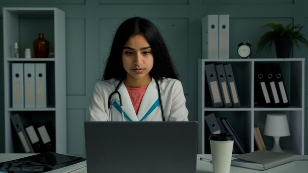 Annoiato giovane donna medico stagista medico femminile lavoro sul computer portatile controllare i risultati dei test dei pazienti