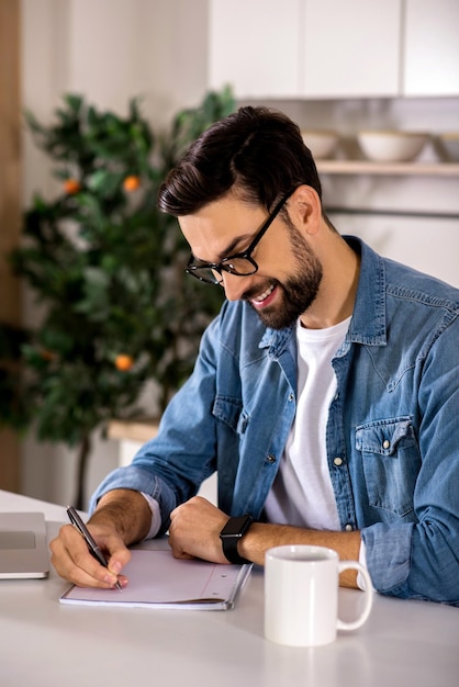 Annotalo Uomo bello allegro che prende appunti e si siede in cucina