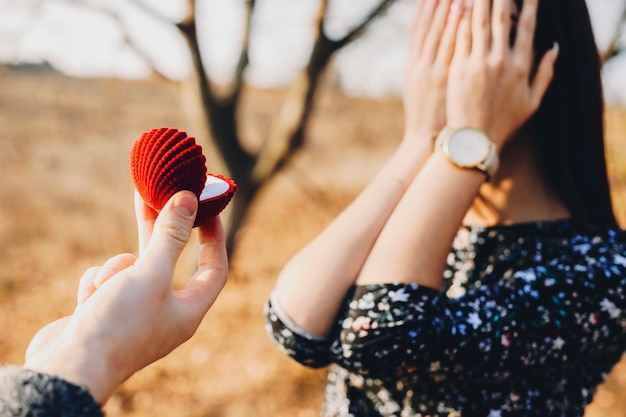 Anonimo giovane donna che copre il viso con le mani mentre si trovava in natura con la mano del raccolto con la scatola dell'anello