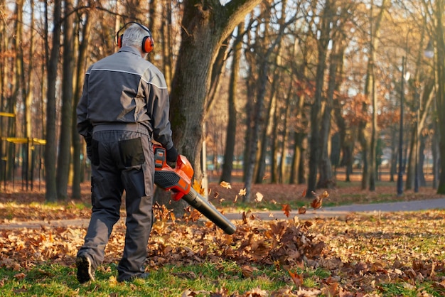 Anonimo operaio comunale maschio che pulisce l'area di riposo in autunno, vista posteriore dell'uomo che indossa