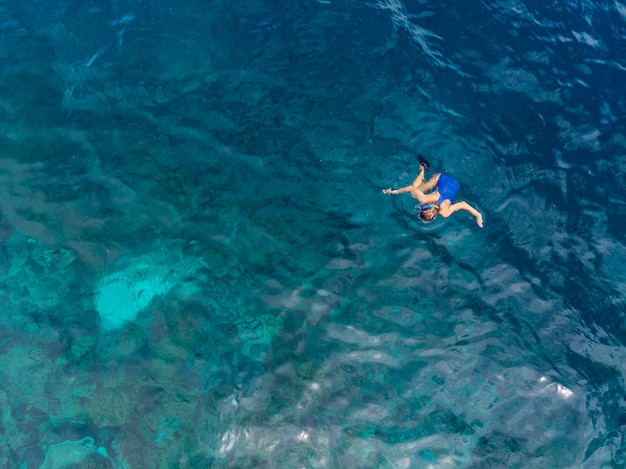 Antenna dall'alto in basso persone lo snorkeling sul mare tropicale della barriera corallina, acqua blu turchese