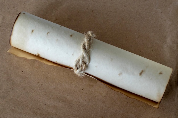 Antica pergamena srotolata di carta beige legata con una corda su uno sfondo marrone