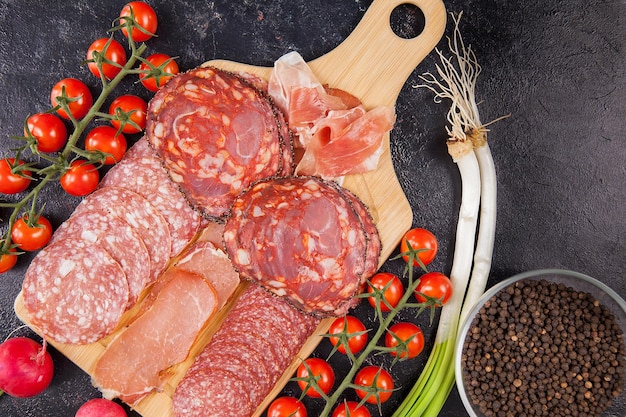 Antipasti di carne accanto a pomodorini, ravanello e cipolla verde