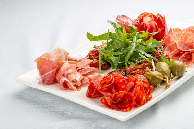 Antipasti di salsicce italiane Prosciutto chorizo pancetta e salame Capperi rucola e pomodori secchi su sfondo bianco