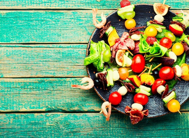 Antipasto a buffet di gamberi, prosciutto, frutta e verdura su spiedini di legno.spazio copia