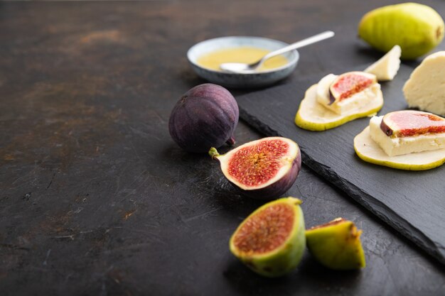 Antipasto estivo con pera, ricotta, fichi e miele sul bordo di ardesia su uno sfondo di cemento nero. Vista laterale, primo piano, messa a fuoco selettiva.