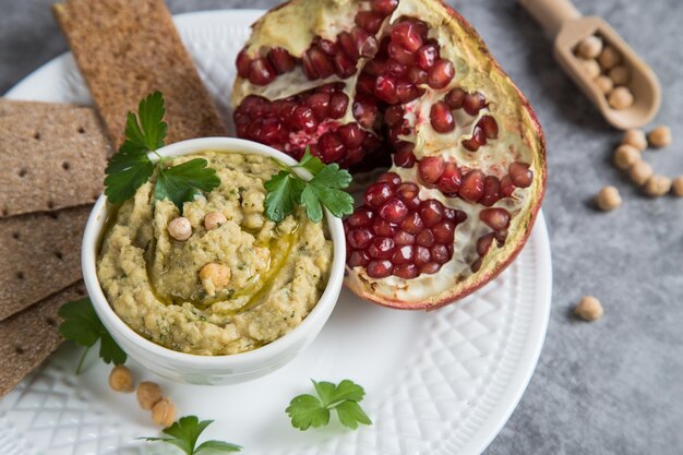 Antipasto hummus di ceci turchi su un piatto bianco con mezzo melograno. Cibo vegano.