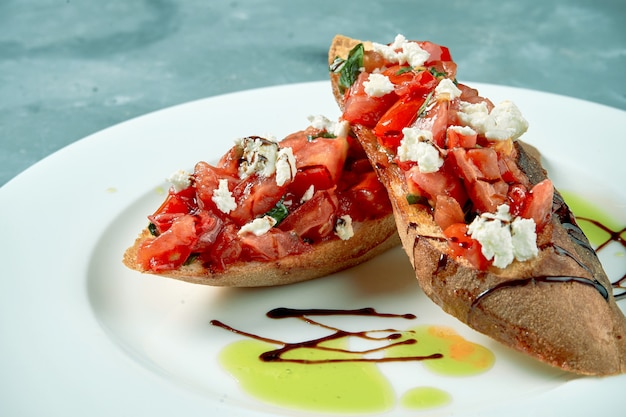 Antipasto italiano. Bruschetta con pomodori e formaggio feta in un piatto bianco su cemento