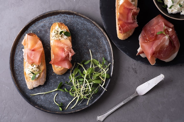 Antipasto italiano di pane e prosciutto, crostini con prosciutto, ricotta e microgreens su sfondo grigio, antipasto.