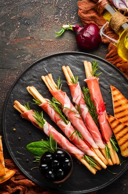 Antipasto italiano Grissini di grissini con prosciutto su un piatto nero Stile rustico Vista dall'alto Spazio libero per il testo