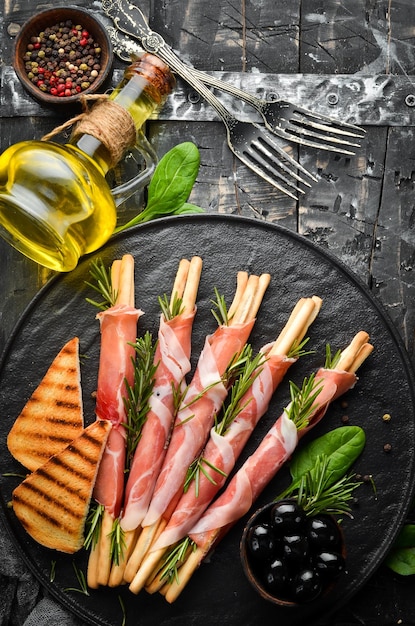 Antipasto italiano Grissini di grissini con prosciutto su un piatto nero Stile rustico Vista dall'alto Spazio libero per il testo