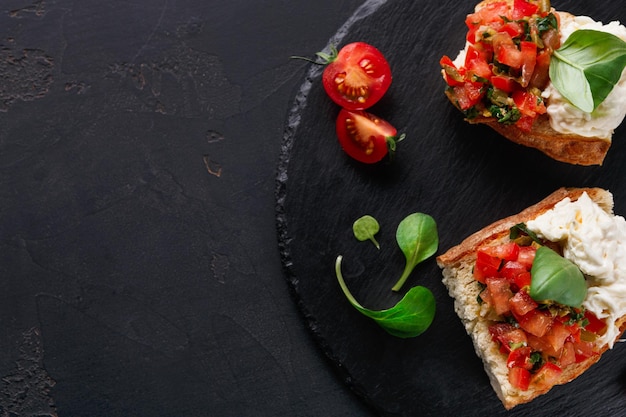 Antipasto italiano su sfondo nero. Bruschetta croccante con pomodorini concasse, stracciatella decorata con spinaci. Pasti al ristorante deliziosi e salutari, vista dall'alto, spazio copia