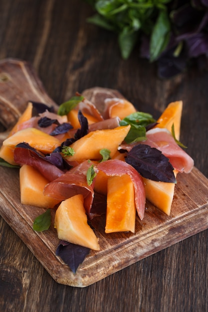 Antipasto, melone con jamon e basilico, su un dochk in legno.