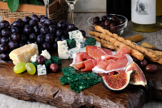 Antipasto su una tavola di legno con prosciutto diversi tipi di formaggio uva e fichi su un tavolo