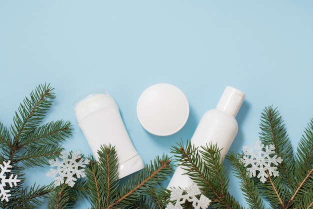 Antitraspirante, gel e crema dei cosmetici di inverno con l'albero verde e fiocchi di neve sull'azzurro, copyspace. cura del corpo