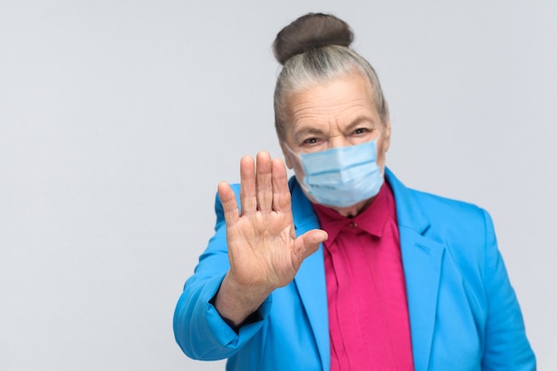 Anziana con maschera medica chirurgica che mostra il segnale di stop alla telecamera