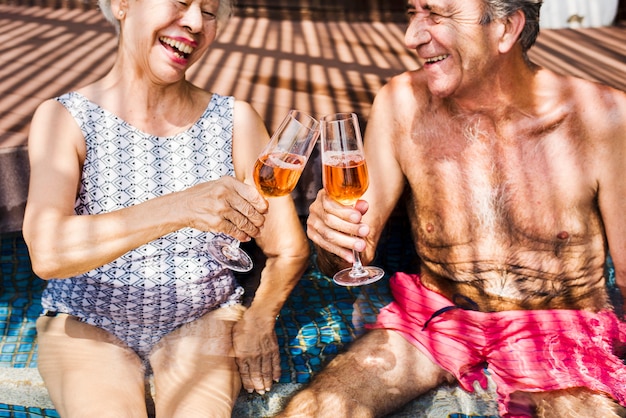 Anziani felici che bevono prosecco in piscina