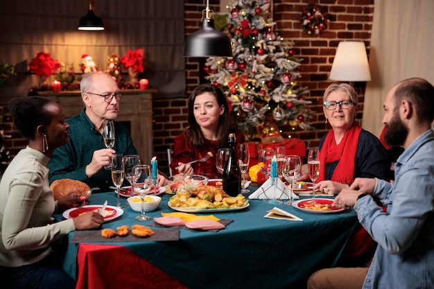 Anziano a cena festiva con gli amici che si godono la celebrazione del Natale a casa, luogo pieno di decorazioni e albero di Natale. La nonna prepara il cibo tradizionale per l'evento delle festività natalizie.