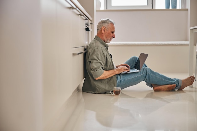 Anziano a piedi nudi che lavora al computer portatile a casa