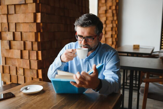 Anziano anziano che legge un libro in una caffetteria godendo il suo hobby letterario