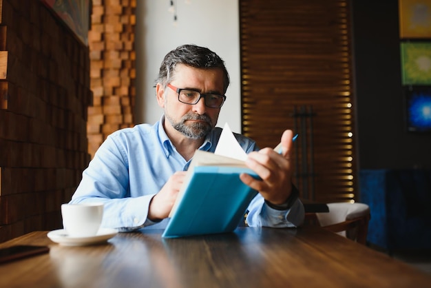 Anziano anziano che legge un libro in una caffetteria godendo il suo hobby letterario