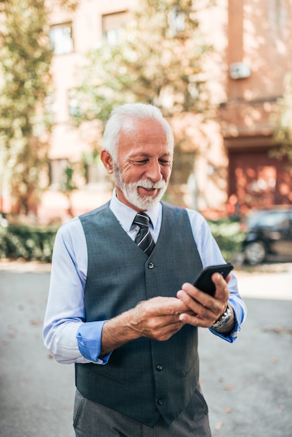 Anziano elegante che utilizza telefono cellulare all&#39;aperto.