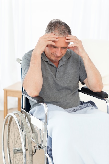 Anziano nella sua sedia a rotelle con mal di testa