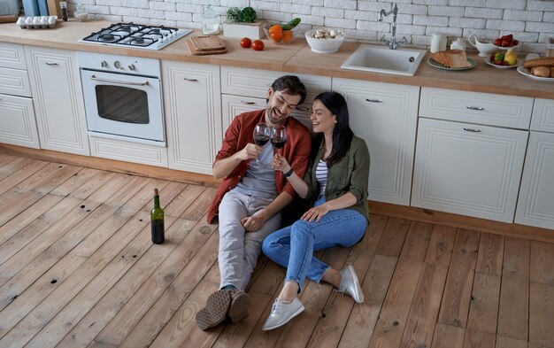 Aperitivo per tutta la lunghezza della giovane bella coppia seduta sul pavimento nella cucina moderna