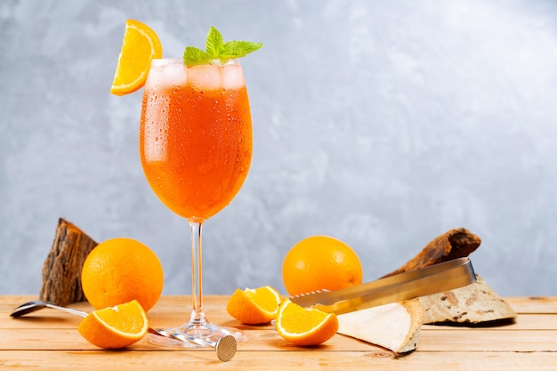 Aperol spritz cocktail con accessori da bar. Cocktail italiano aperol spritz e un'arancia a fette su sfondo grigio. Cocktail aperol spritz con menta fresca