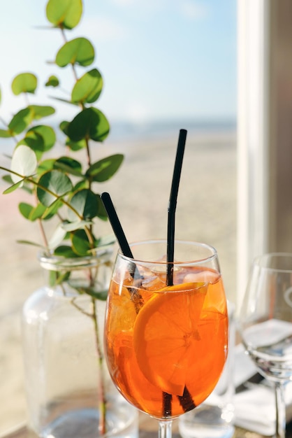 Aperol Spritz e ramoscello di eucalipto in vaso in piedi sul tavolo nella caffetteria sulla spiaggia vicino al mare