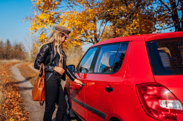 Apertura della portiera della macchina. La donna apre l'automobile rossa con la chiave sulla strada di autunno