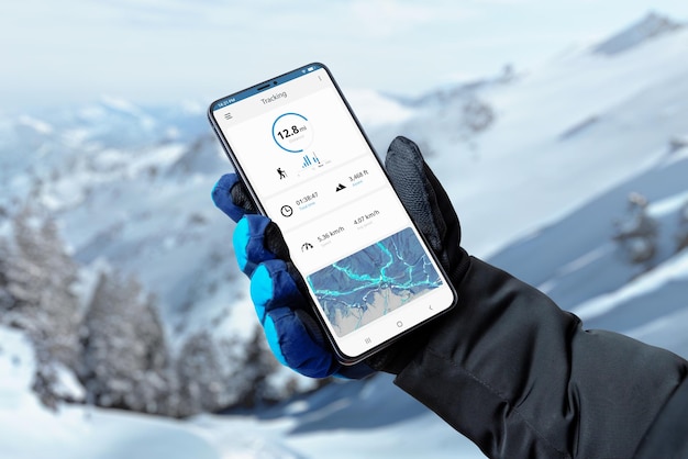 App di tracciamento escursionistico su smartphone in mano all'uomo con guanto Montagna ricoperta di neve sullo sfondo