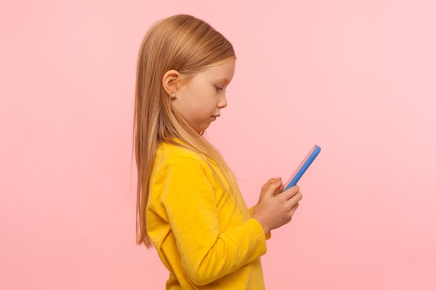 App facile per i bambini. Profilo di bambina positiva che utilizza smartphone, gioca su dispositivo mobile, naviga sul web con espressioni interessate, dipendenza da Internet. riprese in studio indoor, isolate