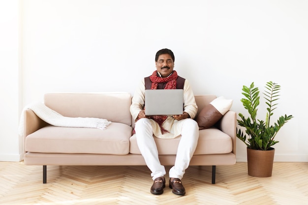 Appaltatore indipendente felice dell'uomo indiano che utilizza il computer portatile a casa