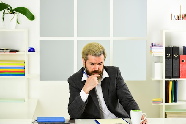 Appassionato del loro progetto insegnante di scuola matura Uomo d'affari di mentalità imprenditoriale in giacca formale si siede al capo del tavolo sul posto di lavoro moderno ufficio vita lavoro a distanza mentre coronavirus quarantena