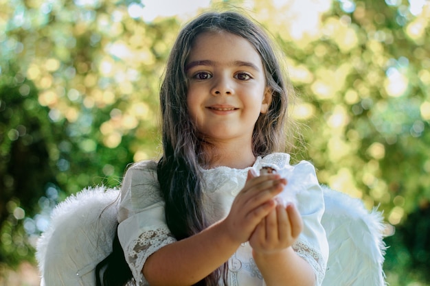 appena battezzata bambina cristiana in abiti da angelo seduta in giardino e sorridente