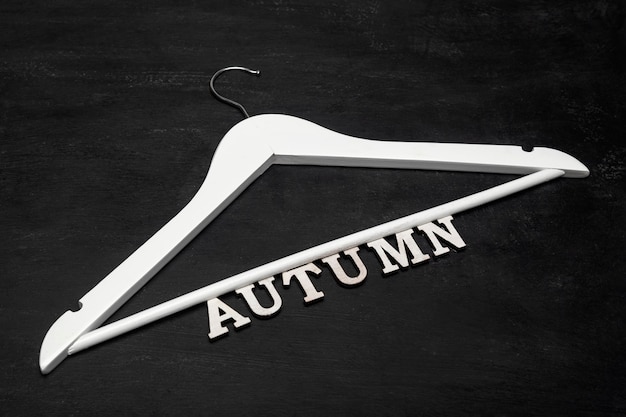 Appendiabiti in legno bianco e scritta AUTUNNO su sfondo nero. autunno concetto di raccolta di abbigliamento.