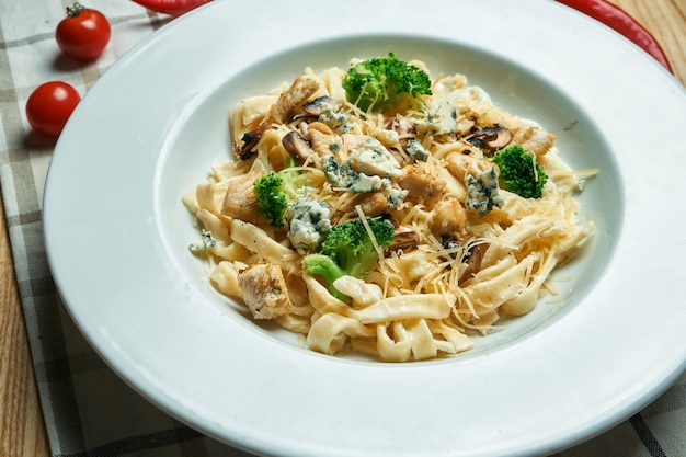 Appetitosa, pasta fatta in casa (tagliatelle) con broccoli, gorgonzola e pollo in un piatto bianco su un tavolo di legno. Cucina italiana tradizionale